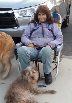 A woman sitting in an aluminum folding chair with her dog.