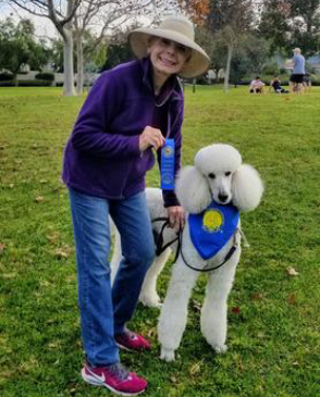 A woman standing next to a white poodle.
