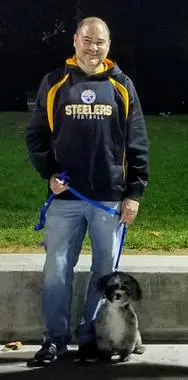 A man standing next to his dog on the sidewalk.